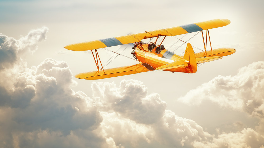 A yellow Texas Biplane soaring above the clouds,, one of the best activities for adults in Houston. 