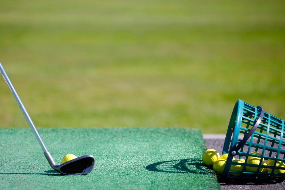 A golf clubs hits yellow practice balls at a driving range at a golf course.