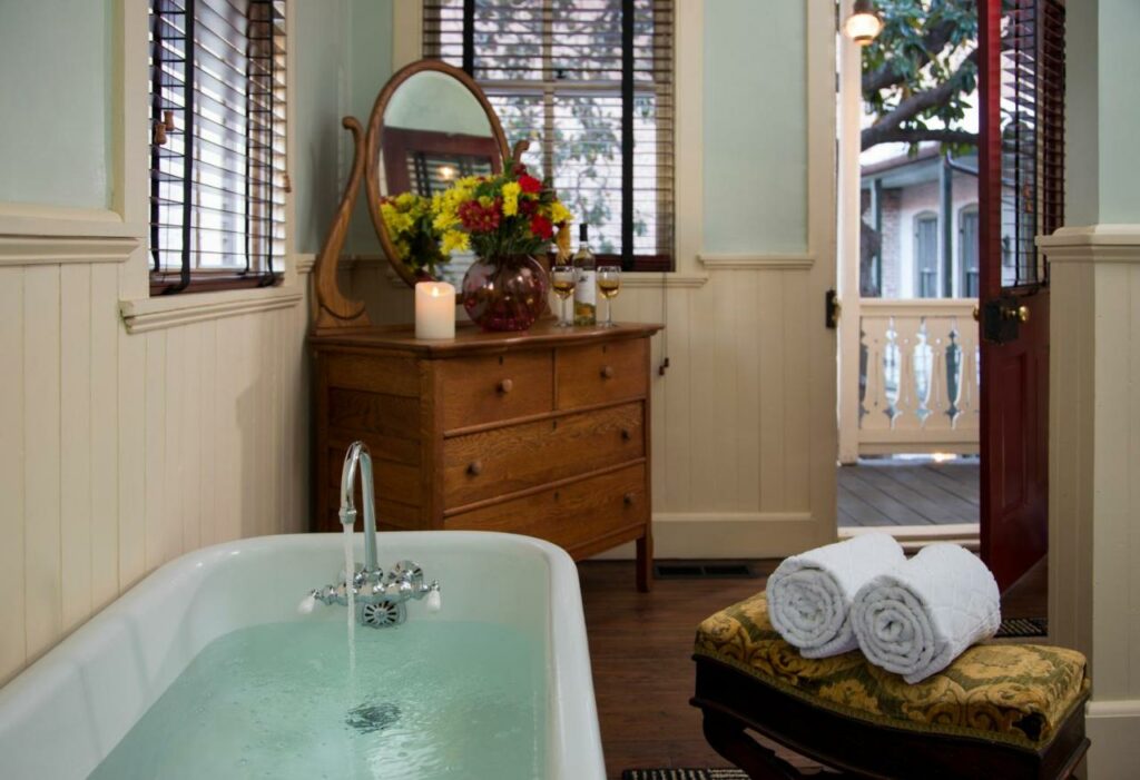 a traditional clawfoot tub with a beautiful wooden dresser, vase of flowers and door open to a balcony!