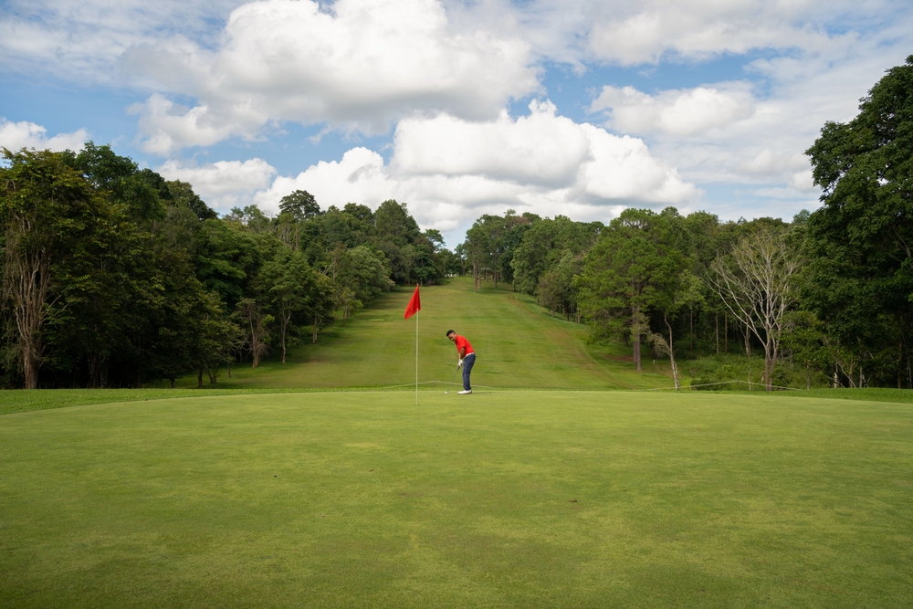 A man in a red shirt i the middle of the fairway on the greens putting 