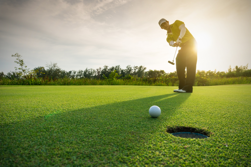 man putting a gold ball into the hole on a golf course, the sun is behind the golfer, one of the best things to do in pass christian