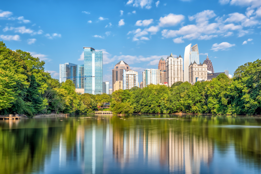 View of Midtown of Atlanta from a park with the city reflected in a lake surrounded by trees. 