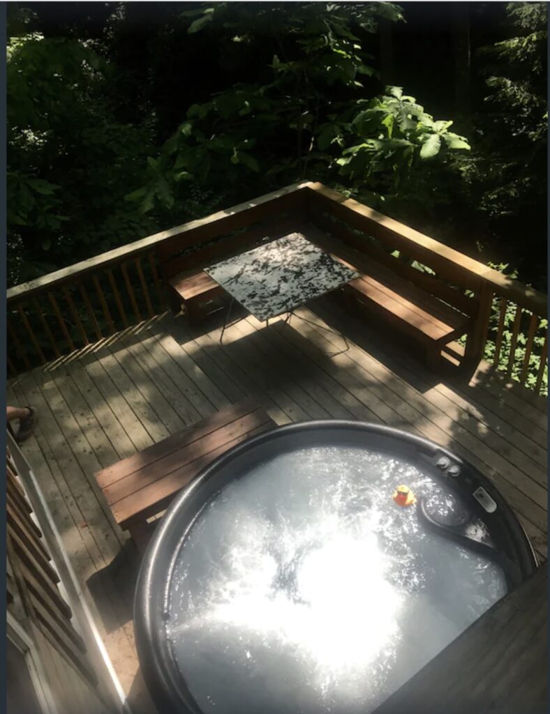 An aerial view from second story looking down on hot tub with a floating rubber duck surrounded by trees on a wooden deck