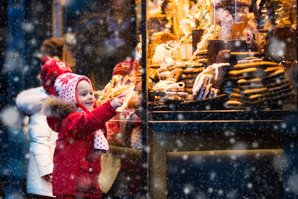 a little girl at a christmas market in Maryland looking at a yummy sweet snack wearing a red coat. 