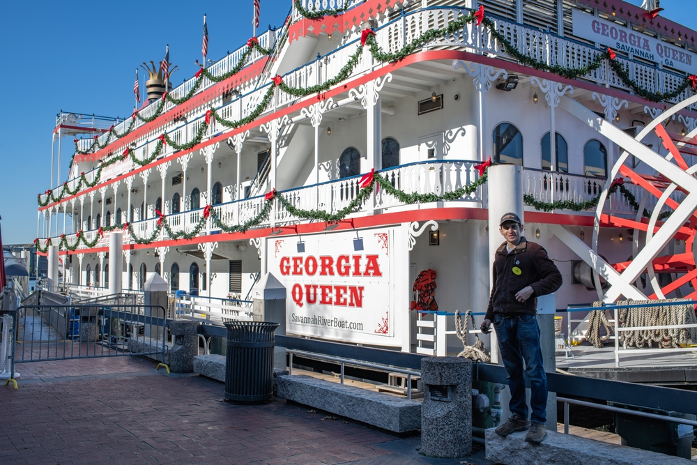 The Georgia Queen Riverboat all decorated for the holiday season with garland and red bows with a man waiting to take your tickets