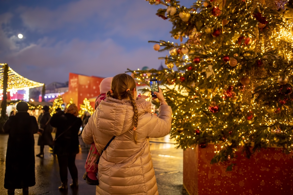 a girl taking a photo of a big christmas tree in Asheville nc 