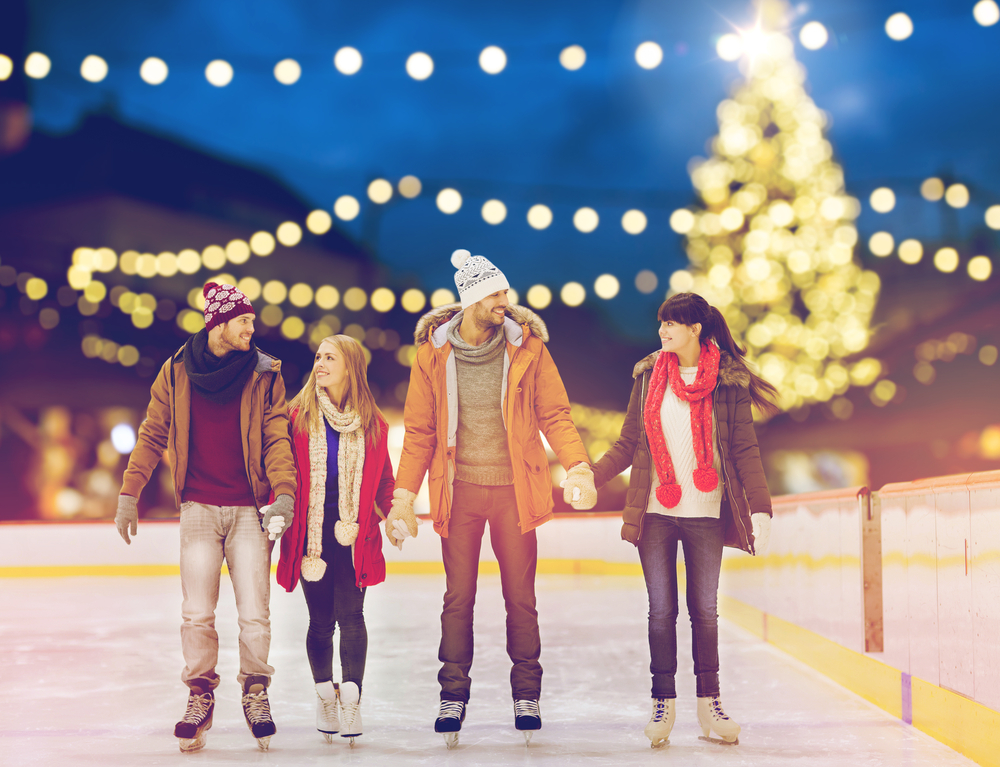 Two couples ice skating with holiday lights and a Christmas Tree in the background at Enchant Christmas, a great Christmas in Dallas activity. 