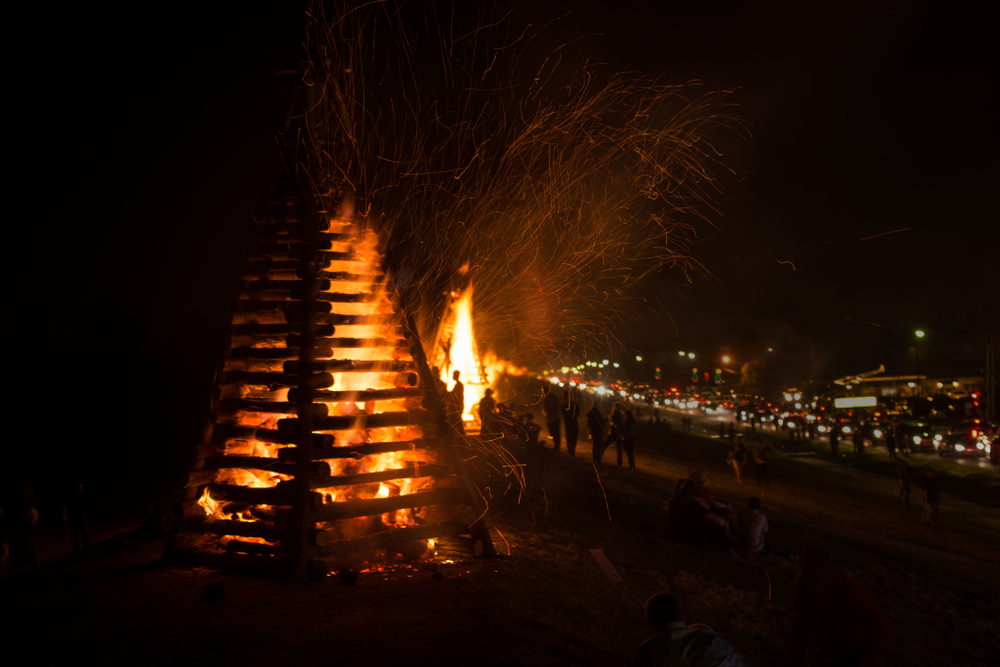 large triangle bonfires are burning along the levee in new orleans for christmas, people stand and sit next to the fires to watch them 