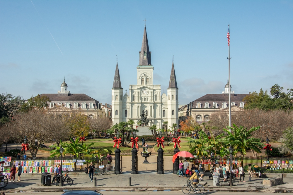 a cathedral in a historic square in Louisiana, christmas decorations are out front and people walk the street in front of the cathedral 