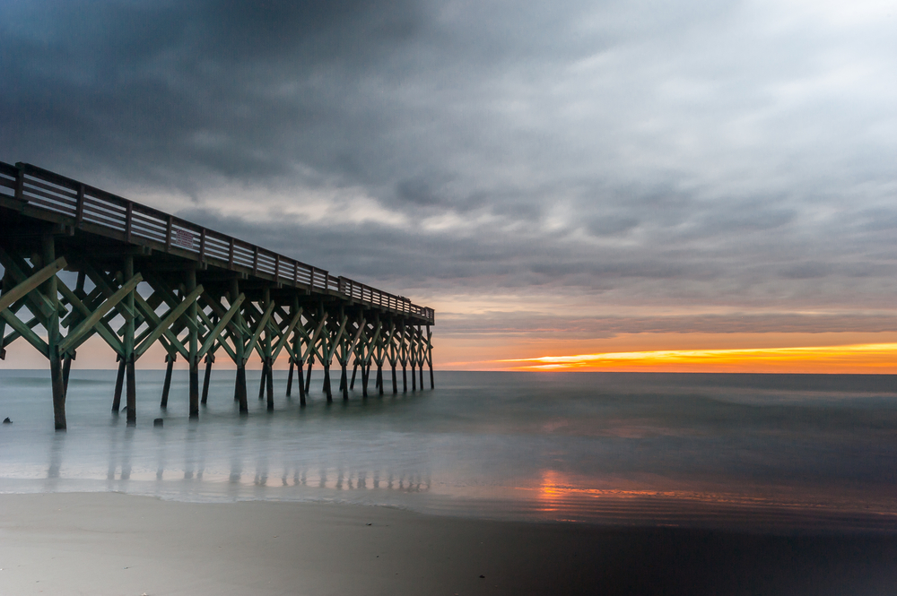 crystal pier at sunrise with calm, flat waters and dark overcast clouds 