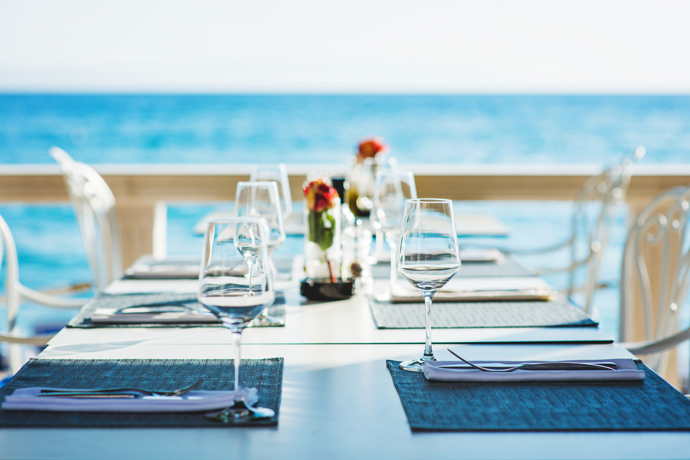 a long table with fine dining glassware set on the table with an ocean view during the day 