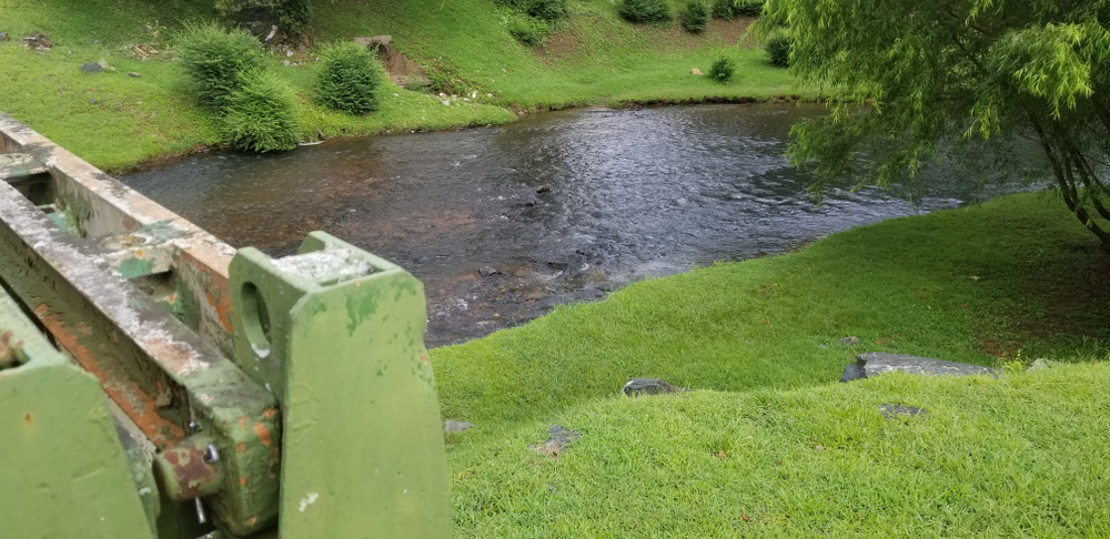 a wide flat river with calm water, green grass on both sides of the river, a bridge to the left 