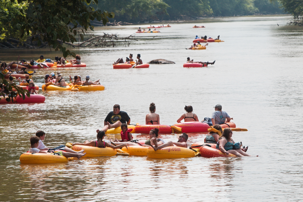 more than twenty people in tubes on a river, trees on both sides of the river