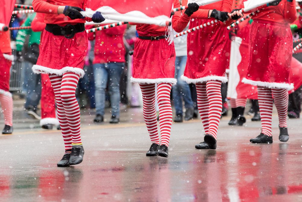 people walking dressed in holiday festive outfits like Santa suits and red and white stockings on a wet street, what you might find while spending Christmas in Charleston 