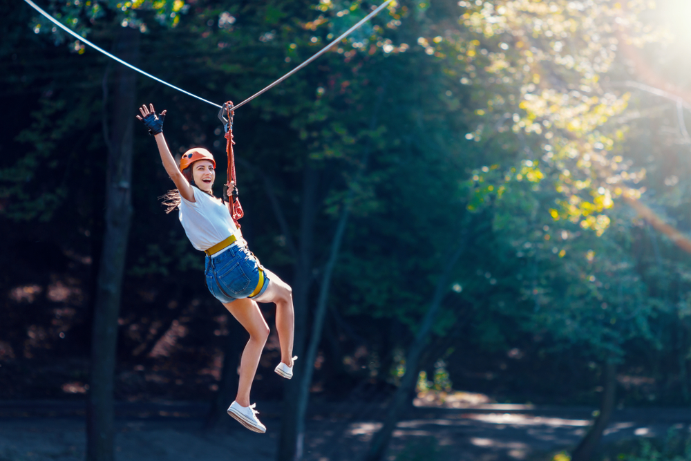 a girl in jean shorts and a white top wearing an orange helmet flying though the zip line in Arkansas 