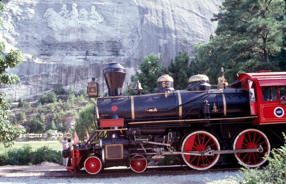 An old-fashioned red and black steamer train chugs past the large rock face of Stone Mountain, one of the best Christmas towns in Georgia.