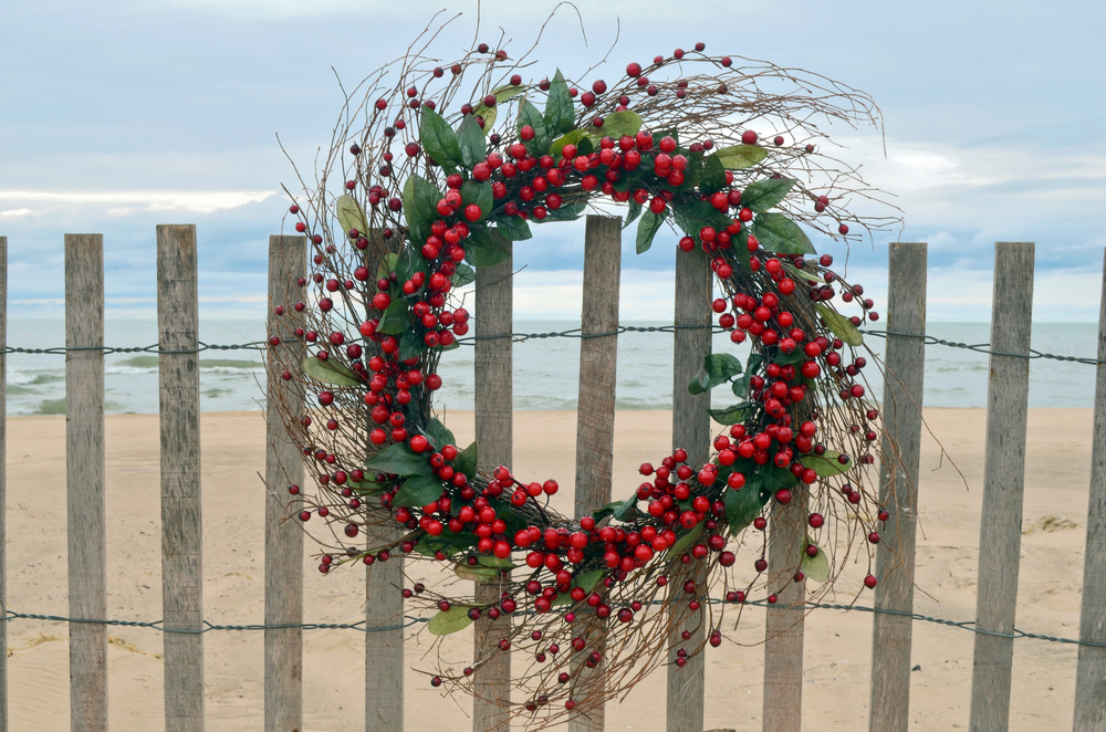 Holly wreath hanging on a fence with the Atlantic Ocean in the background in one of the best Christmas towns in South Carolina.