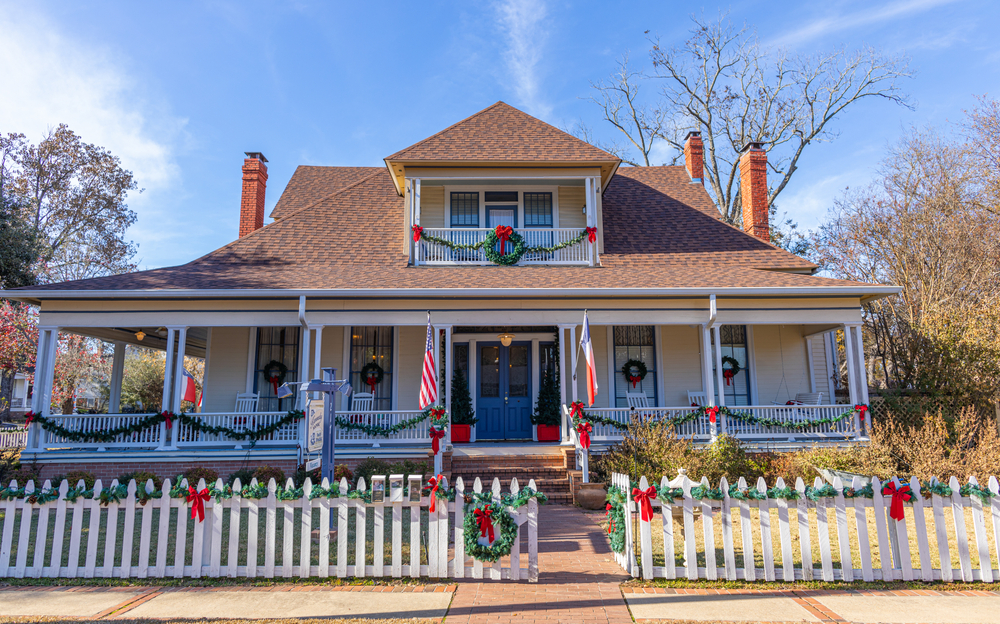 a lovely home with a wrap around porch and balcony decorated in beautiful holiday wreaths and bows.