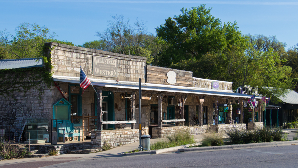 A western building fit for a rodeo, decorated with various flags and beautifully constructed out of old stone and blue painted trim!