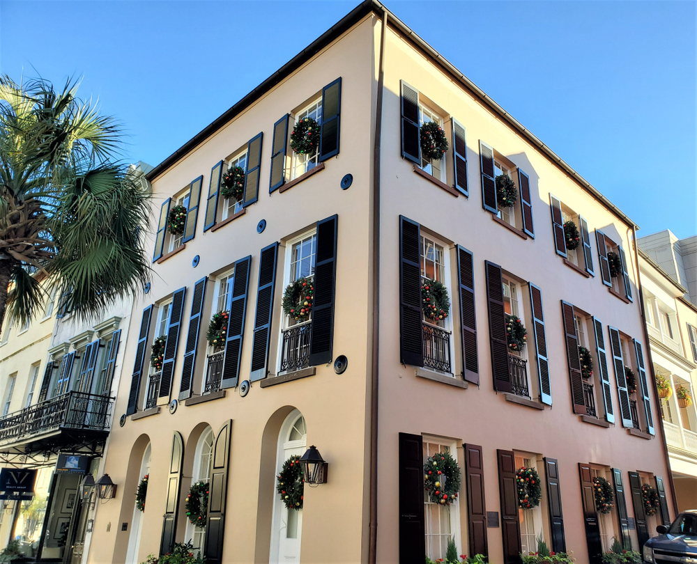 Building in historic Downtown Charleston that has a wreath with gold and red ornaments hanging from every window and door of the 3-story building on a bright sunny day 