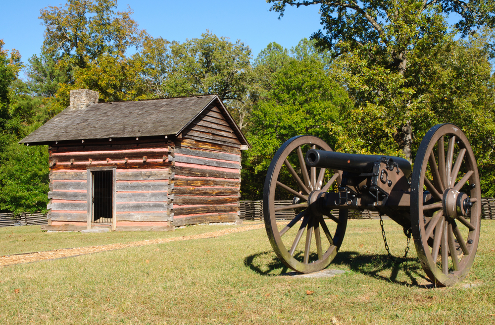 A cannon and cabin located at Chickamauga Battlefield on a sunny day with trees surrounding the area. This is one of the civil war battlefields in Georgia that is the largest in history. 