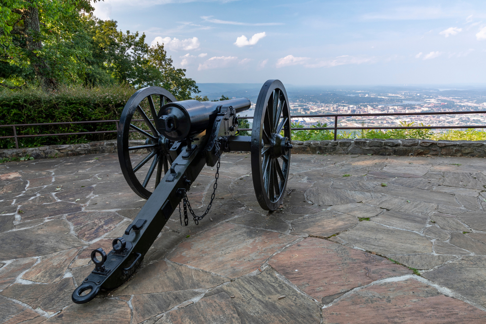 civil war cannon on an overlook with a view of a city in the background with a cloudy haze in the sky