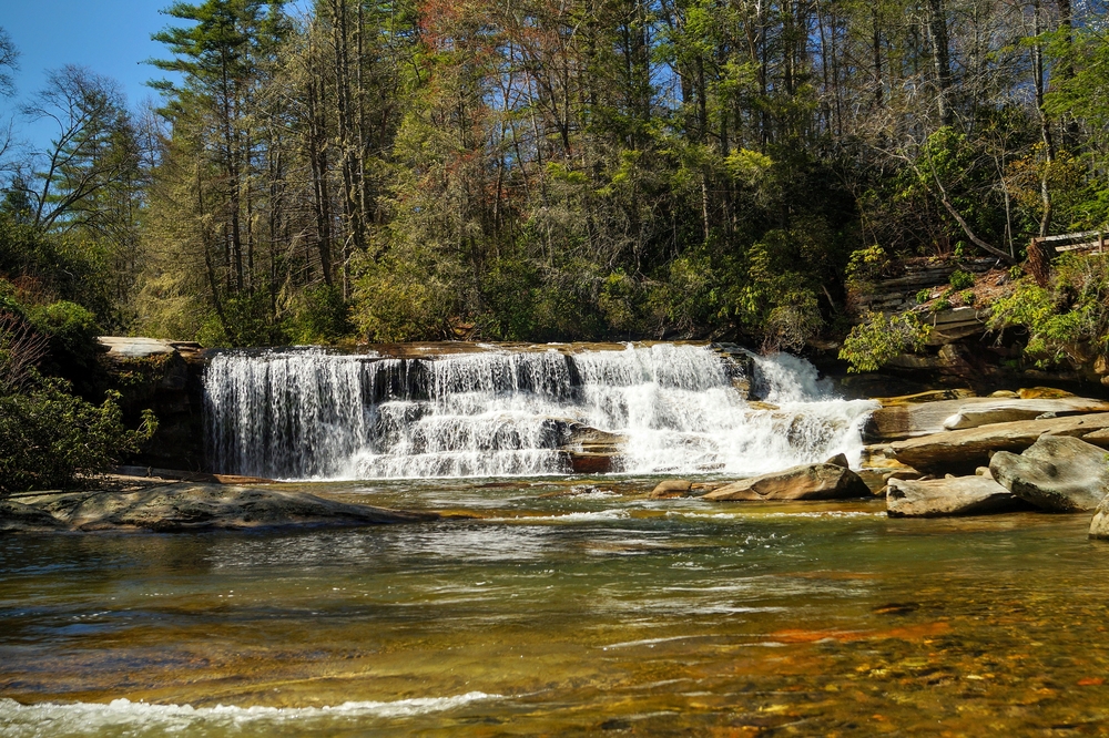 Waterfalls over rocks with big trees and a bit of a shallow area, a good spot to stop for a swim and a stretch while river tubing in North Carolina!