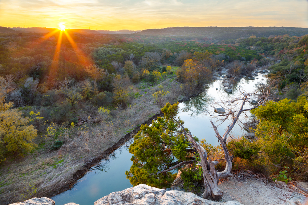 The sun sets over the Greenbelt, a peaceful area with trees and a creek.