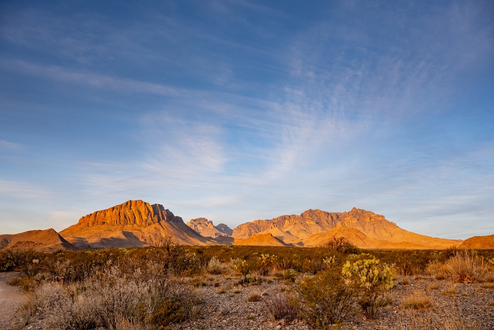 The sun hits the Chisos Mountains, making them glow orange against a blue sky.