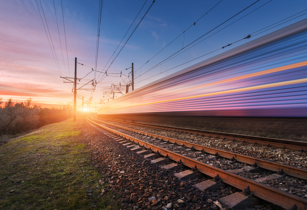 The blur of a train speeds by at sunset along rail road tracks, similar to the high speed train that's being built for those living in Texas.