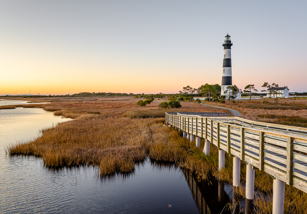 a lighthouse, resting on a swampy area of land with a wooden boardwalk to lead you through a cool area of land!