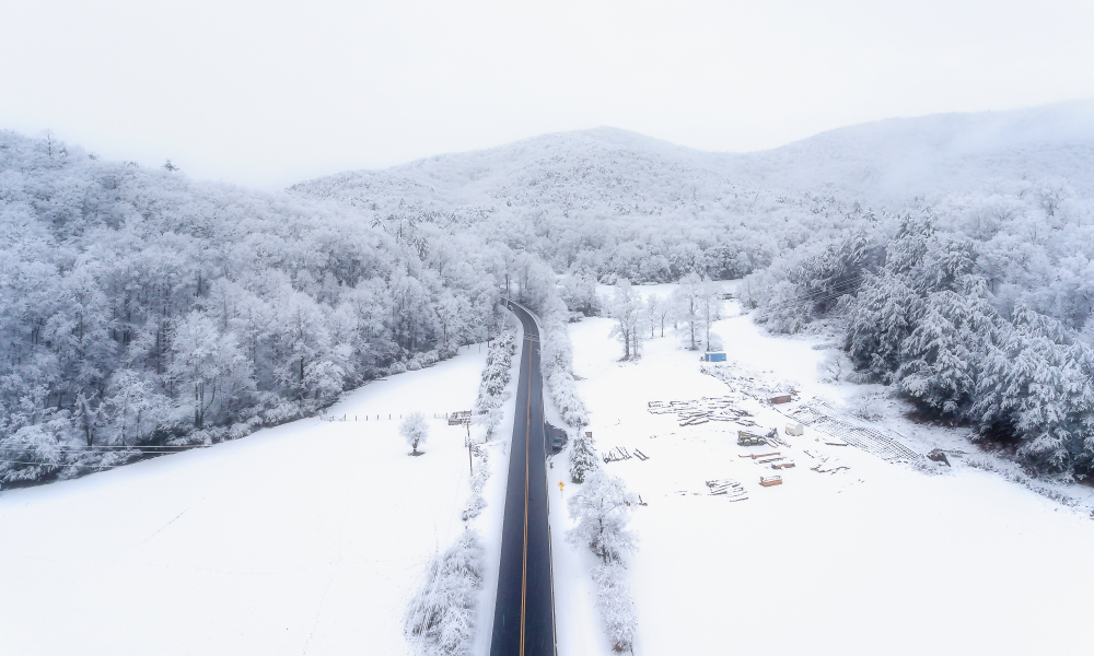 a straight road leading into the mountain before it turns at the end, the road is surrounded by snow and the trees are covered in ice and snow 