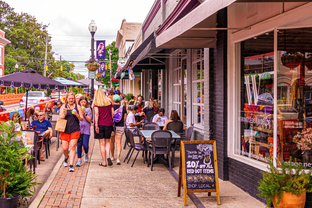 A busy high street with people eating at a restaurant.   