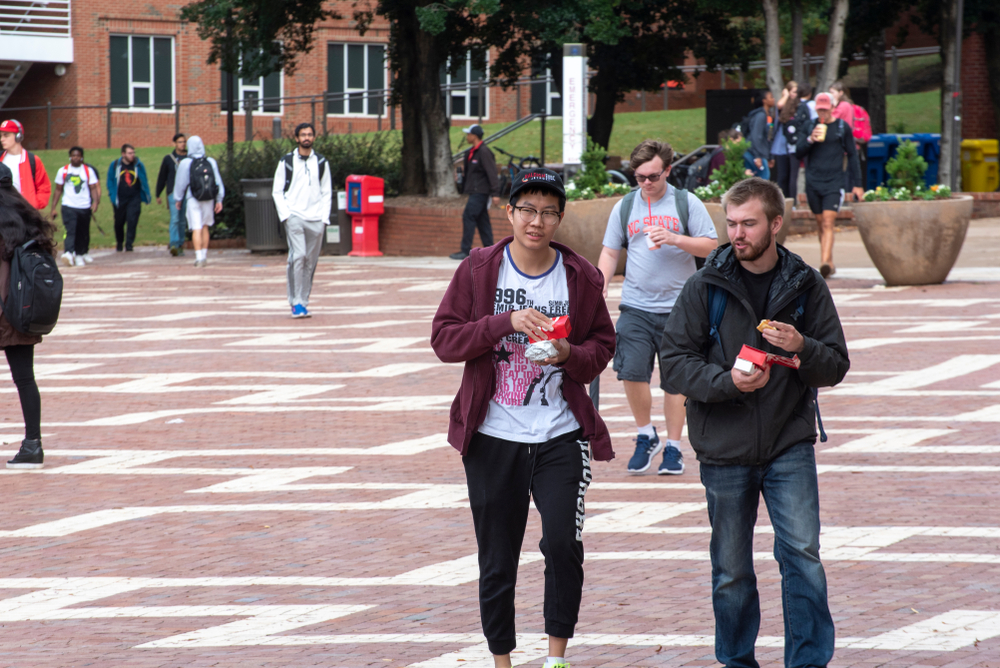 A diverse group of students walk across the campus of North Carolina State University. The article is about living in North Carolina.  