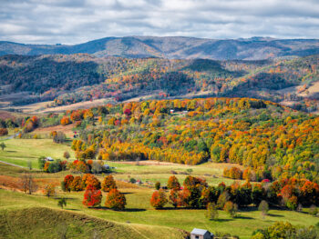 an aerial image of shenandoah mountain ranges in the fall - orange, green, yellow and red trees with the shadows of clouds over the range