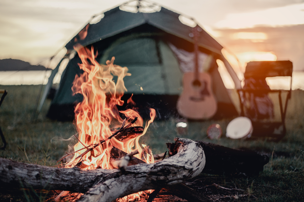 a beautiful fire, guitar, and tent sitting in the sunset along the beach 