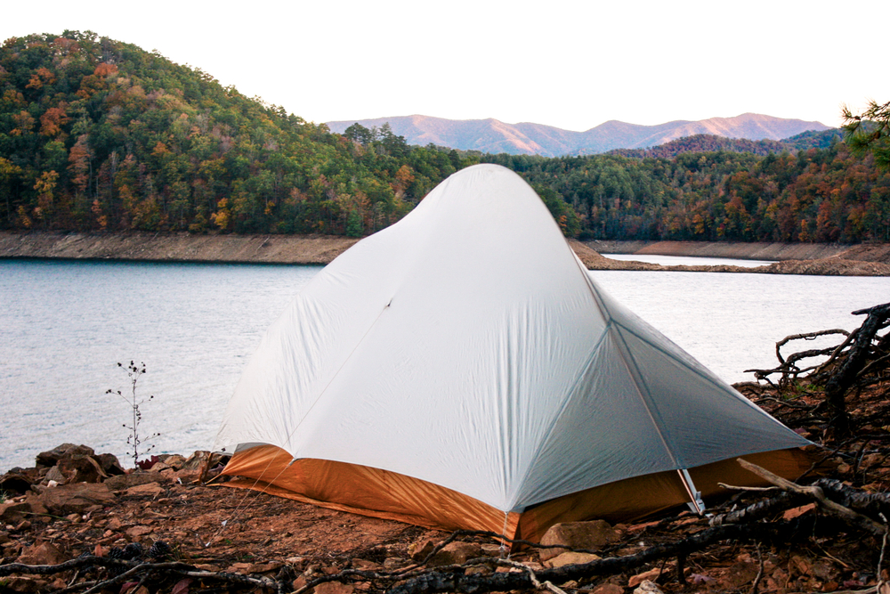 a white and orange tent on the edge of a lake with pretty mountains in tieback 