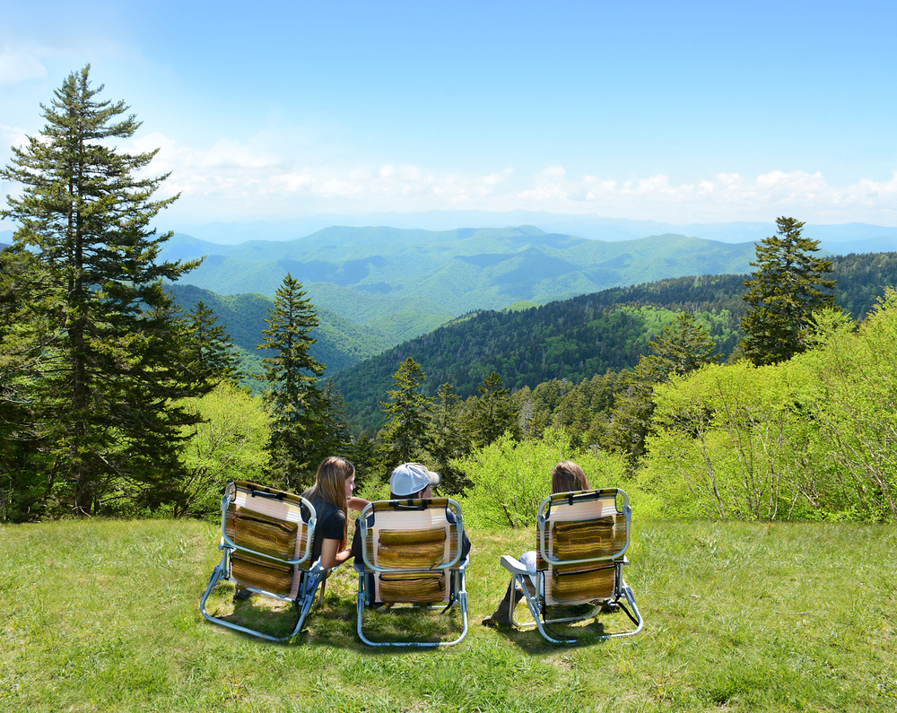 three people sitting on the edge of a mountain side with the beautiful blue ridge mountians in the distance. 