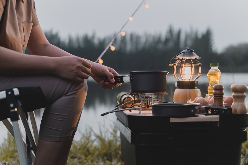 a women cooking her camp fire by a lake in North Carolina she has pretty lights and all the best camping supplies 