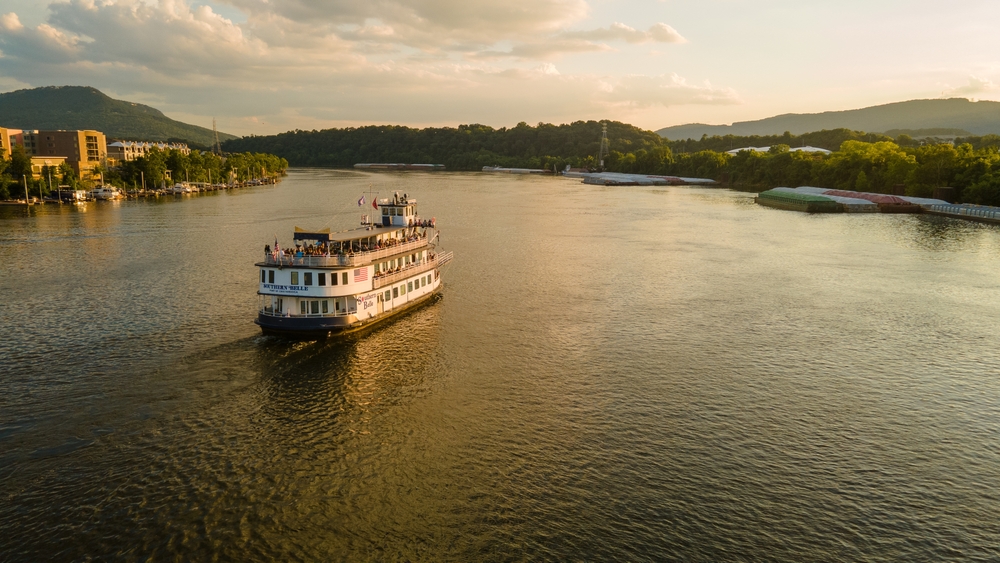 a big river boat on the mississippi river at sunset with mountains in the back round a small town on the riverbank