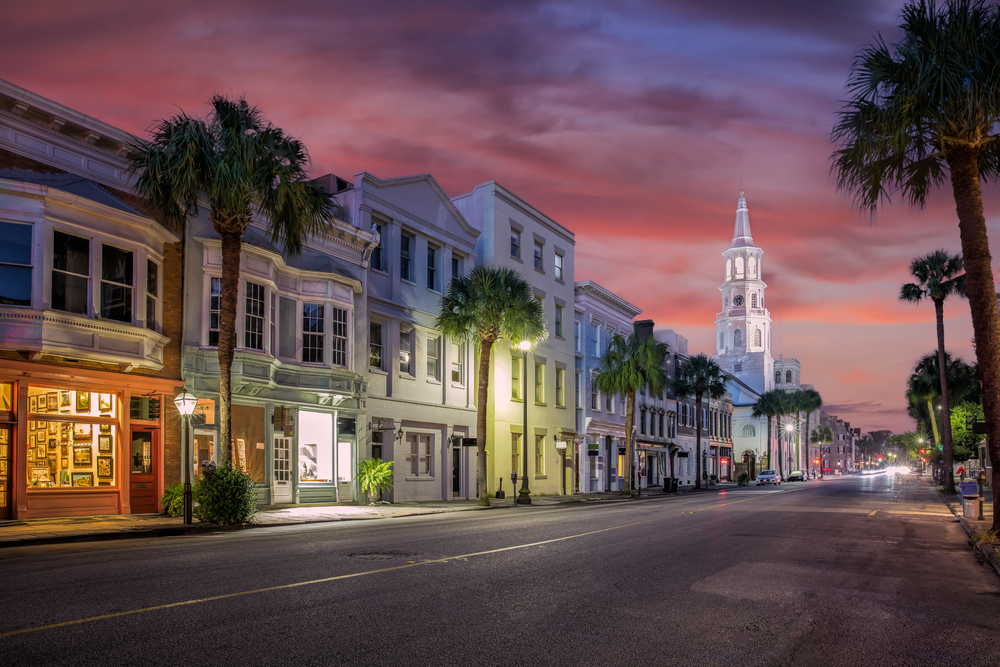 Purple dusk over downtown Charleston with palm trees and a white church.