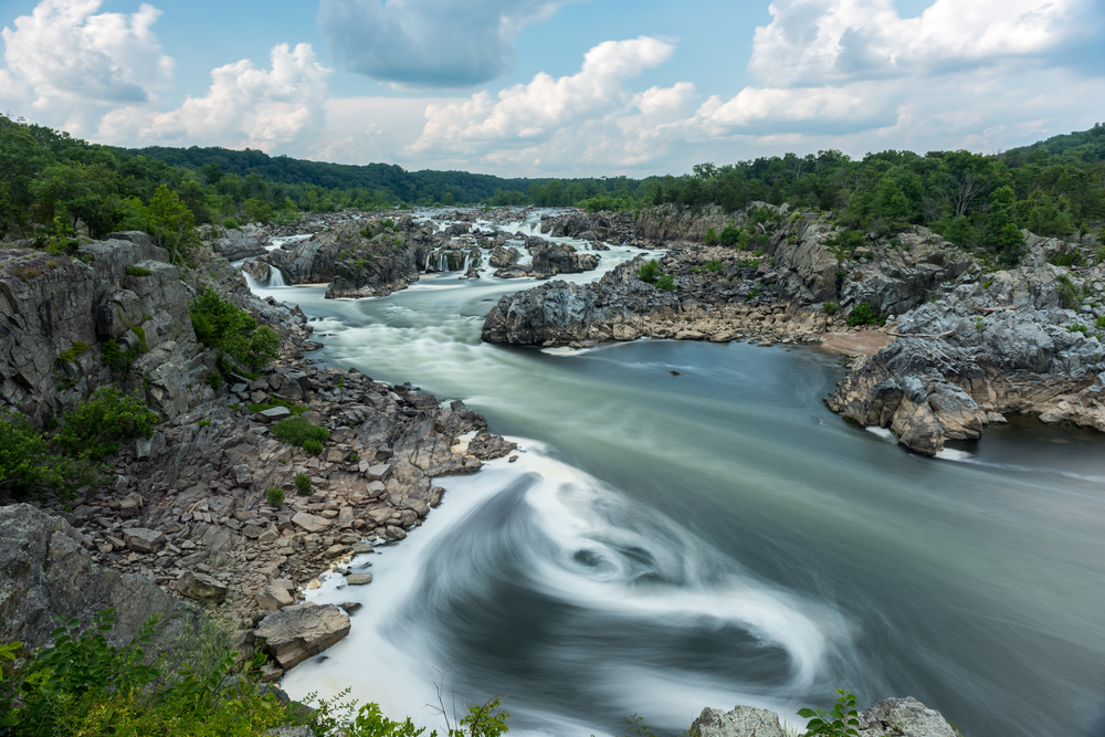 A view of a wide multi-cascading waterfall in a large river with rocks sticking out of it in several sections