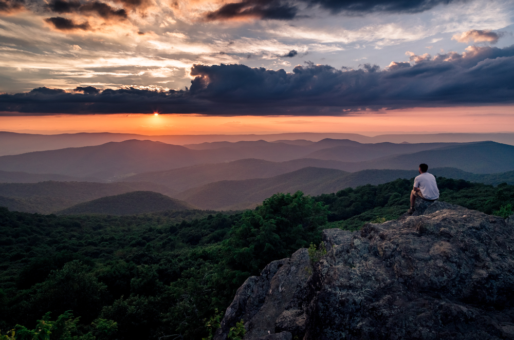 a lovely view of a sunset hike in harrisonburg. there is someone sitting on the edge of the cliff looking at the sun go down this is one of the best things to do in harrisonburg VA 