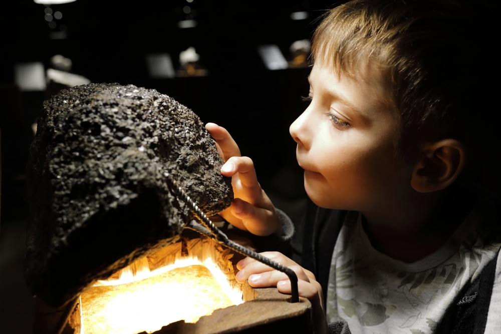 a little kid looking at a mineral inside the Mineral Museum in harrisonburg. they have their fingers touching the deposit and look very interested 