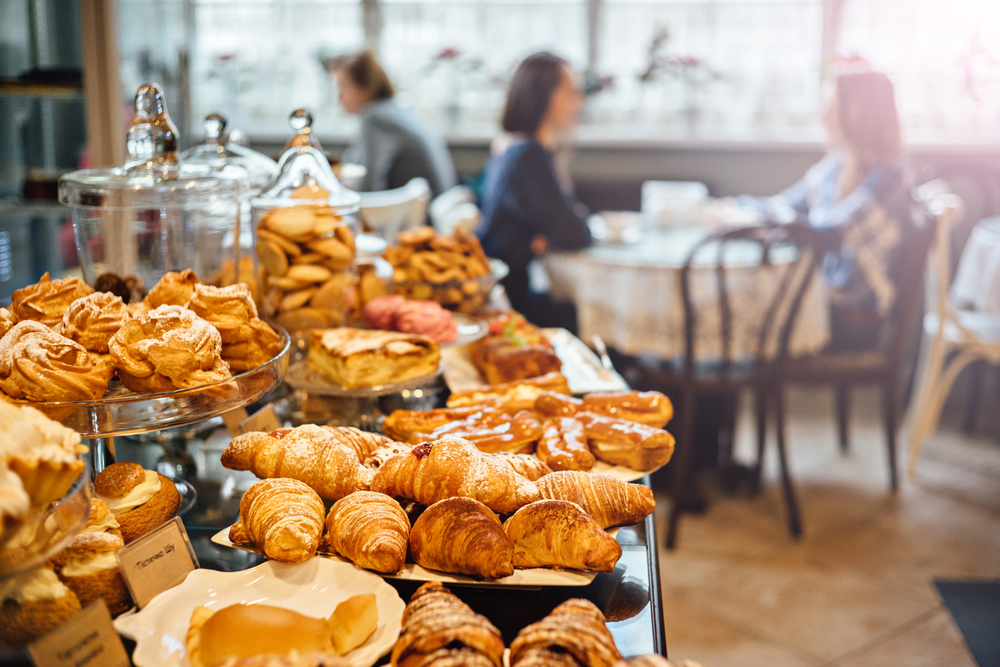 a bunch of flakey desserts in one of the best cafes in harrisonburg . you can see people eating in the back round and so many choices for breakfast 