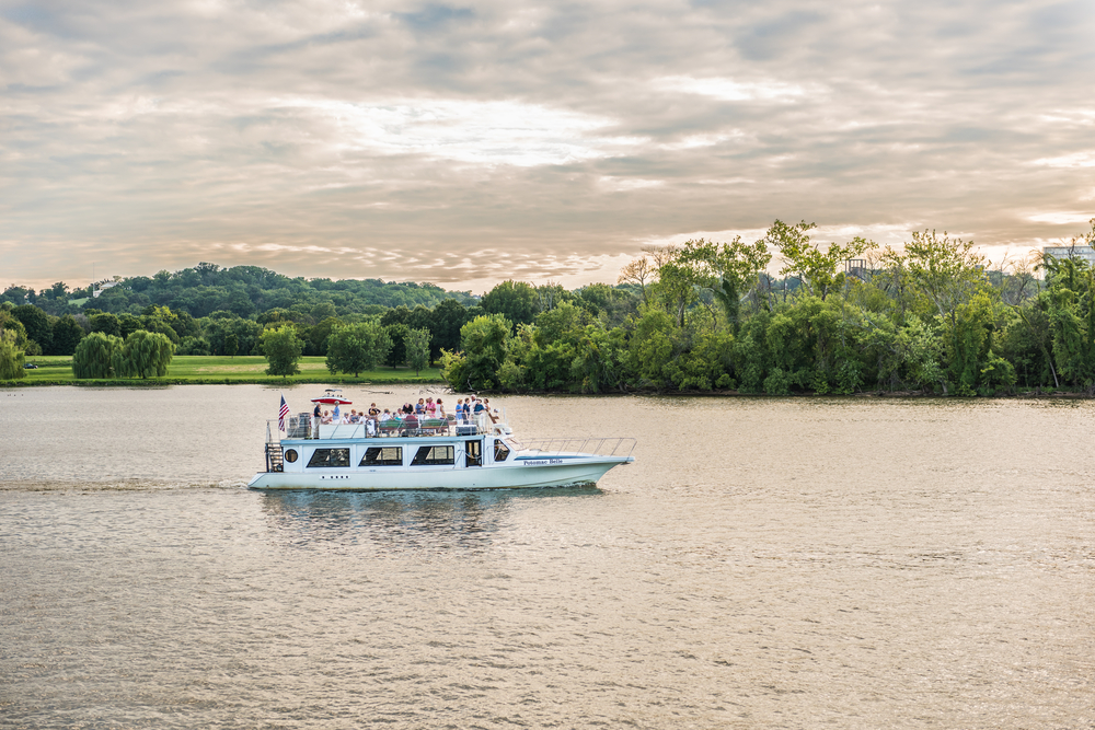 White cruise boat with people on top going down the Potomac River at sunset.