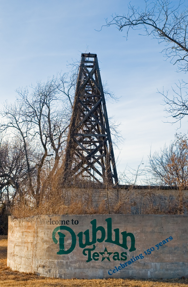 a concrete wall that says welcome to dublin texas celebrating 150 years, a large wooden tower can be seen in the background,places in the South USA that look like Europe