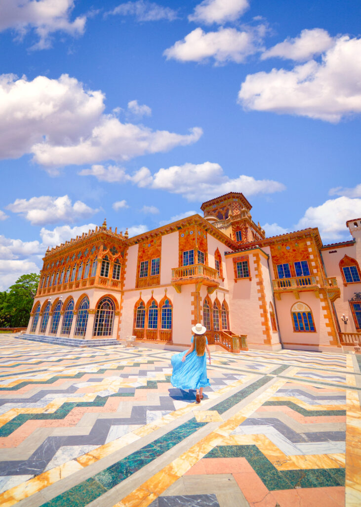woman in a blue dress on a mosaic tile deck outside of an ornate building on a partly cloudy day