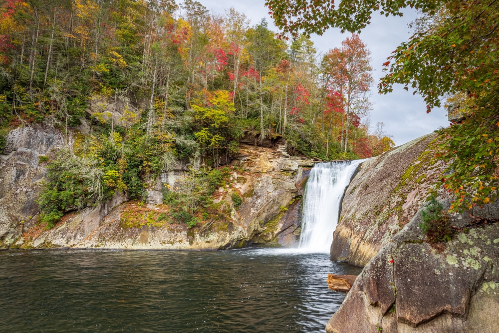 a curved rock wall around a pool of water beneath a waterfall in the mountains of north carolina, photo taken in the fall 