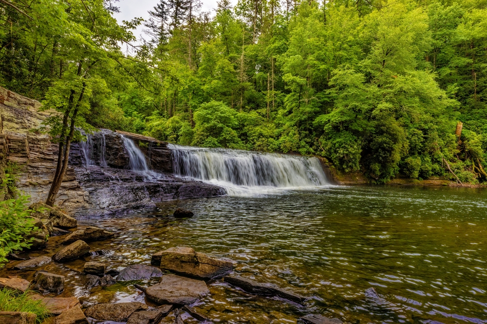 swimming holes near asheville, hooker falls dumps into a pool of water below, the trees are full, photo taken in the summertime 